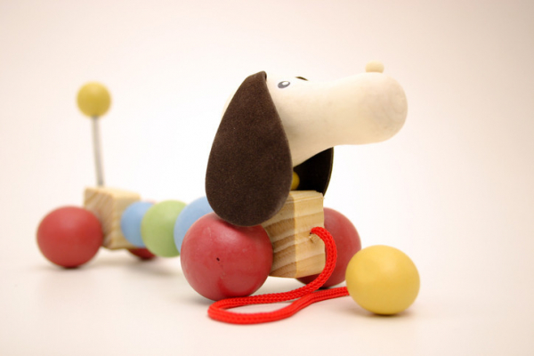 photo of a colorful wooden dog pull toy with long brown ears, round red balls for feet, and a yellow ball at the end of its tail